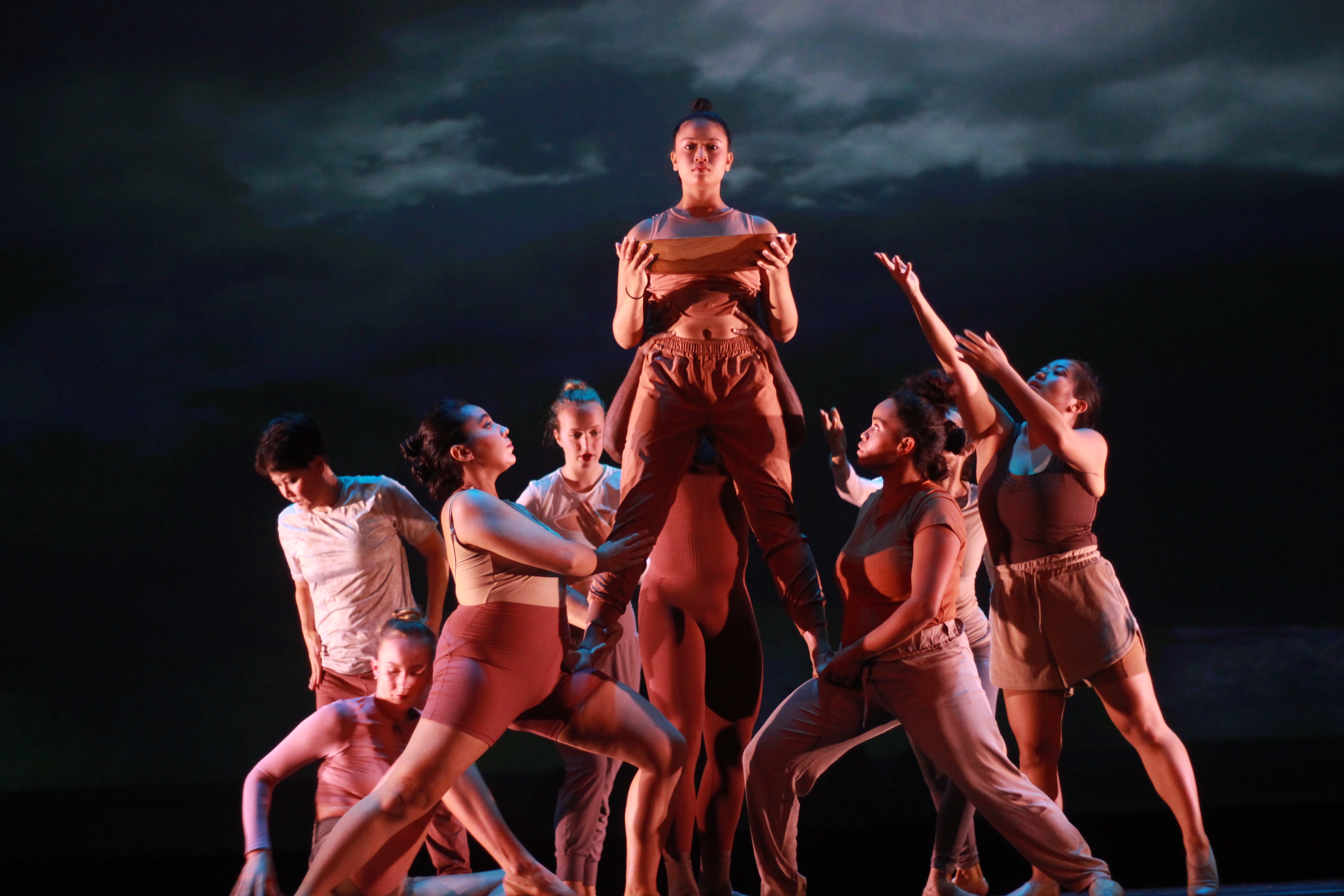 Dancers in a cluster in front of stormy sky